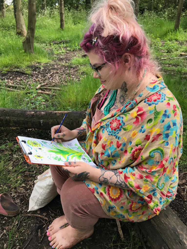 woman wearing colourful clothes sitting peacefully in the woodland drawing and painting nature